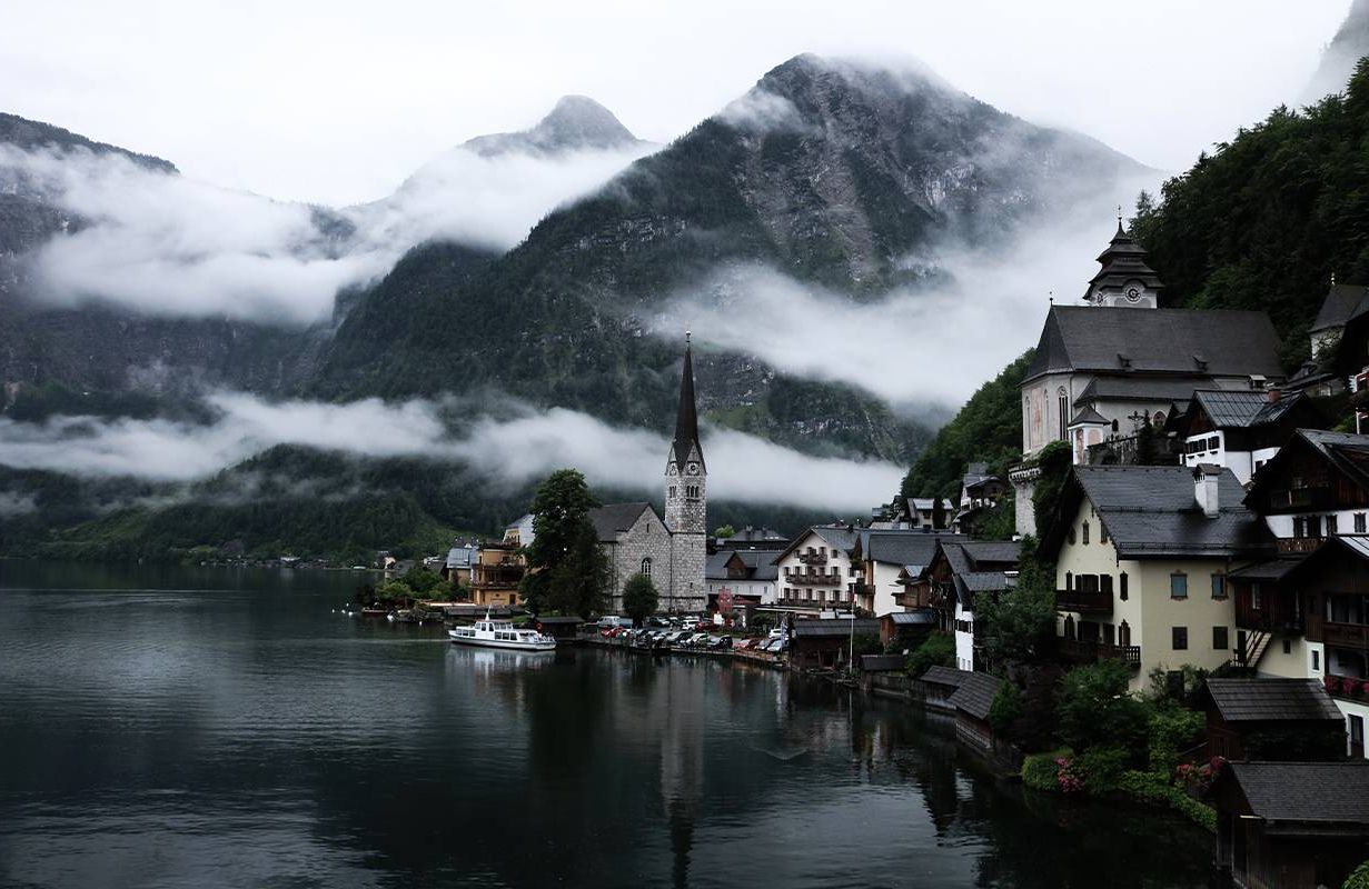 A landscape view of a small town on a lake with mountains in the background on a cloudy day. Next Avenue