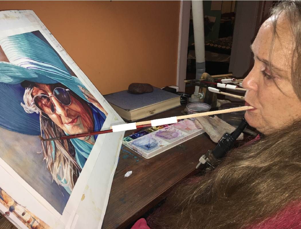 A closeup photo of a woman painting by holding a paintbrush in her mouth. Next Avenue