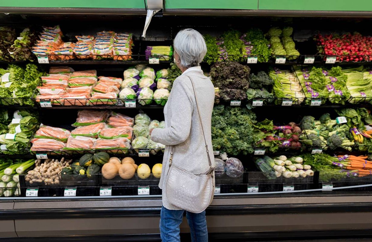 An older woman looking at vegetables at a grocery store. Next Avenue