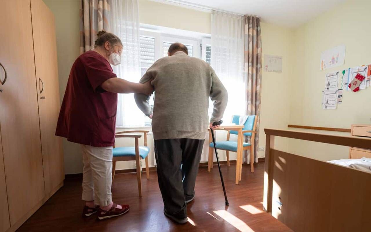 A staff member at a nursing home helping a patient into a chair. Next Avenue