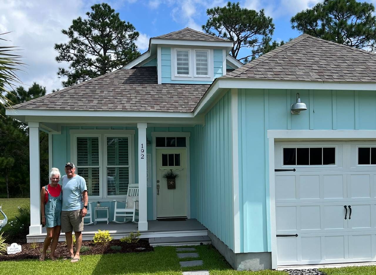 A couple standing in front of a bright blue house. Next Avenue, solar, retirement