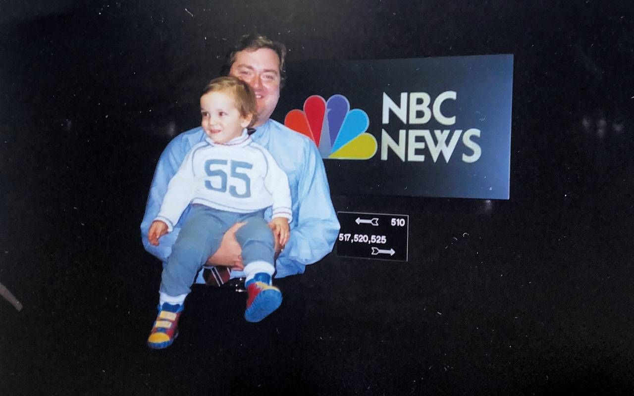 A man holding a toddler in front of a NBC news sign. Next Avenue, Tim Russert