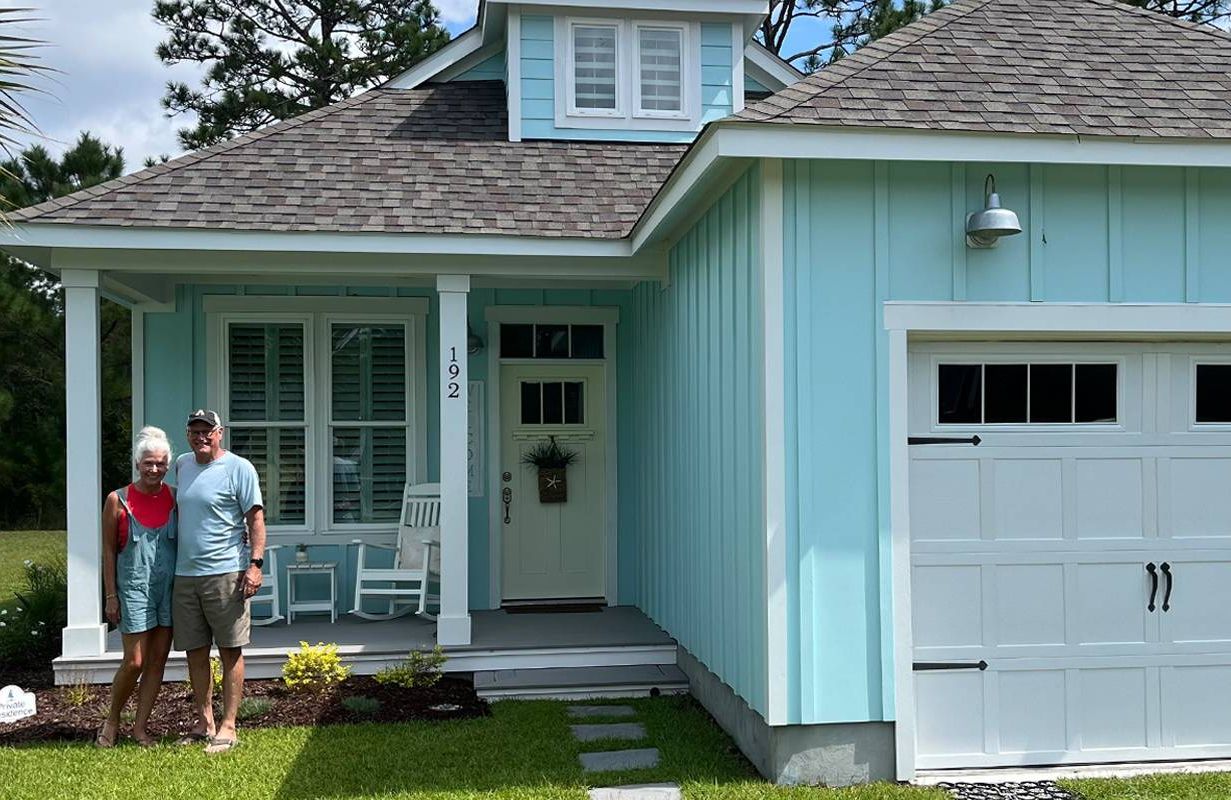 A couple standing in front of a bright blue house. Next Avenue, solar, retirement