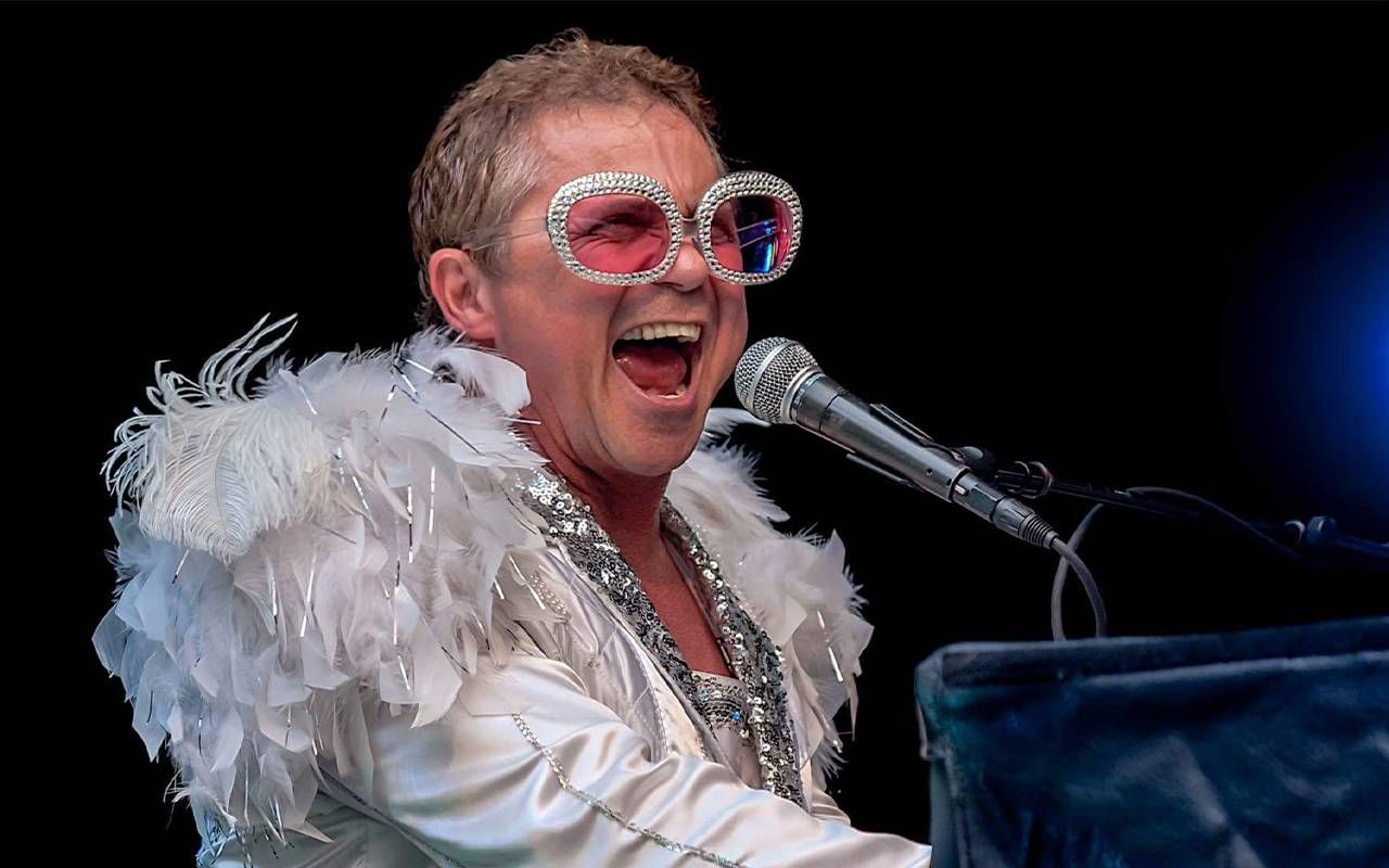 A man on stage wearing an Elton Jon costume. Next Avenue
