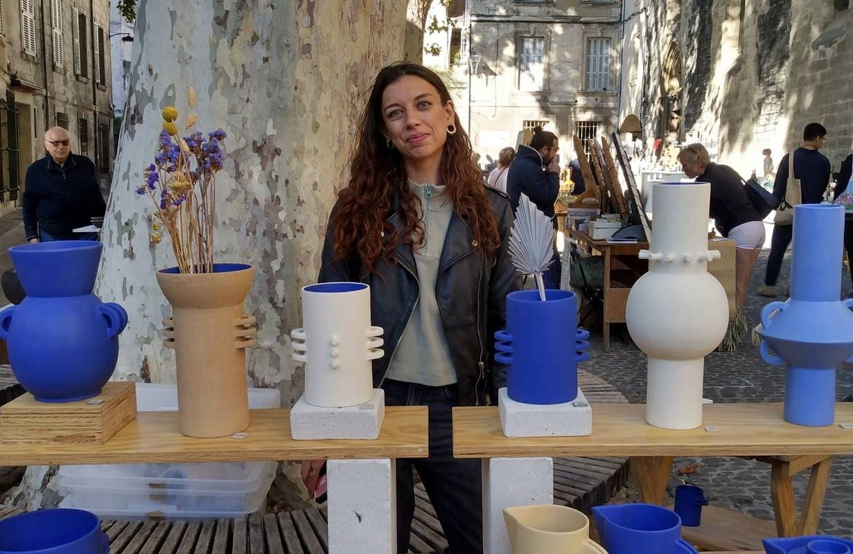 A person smiling in front of various ceramic vases. Next Avenue, france