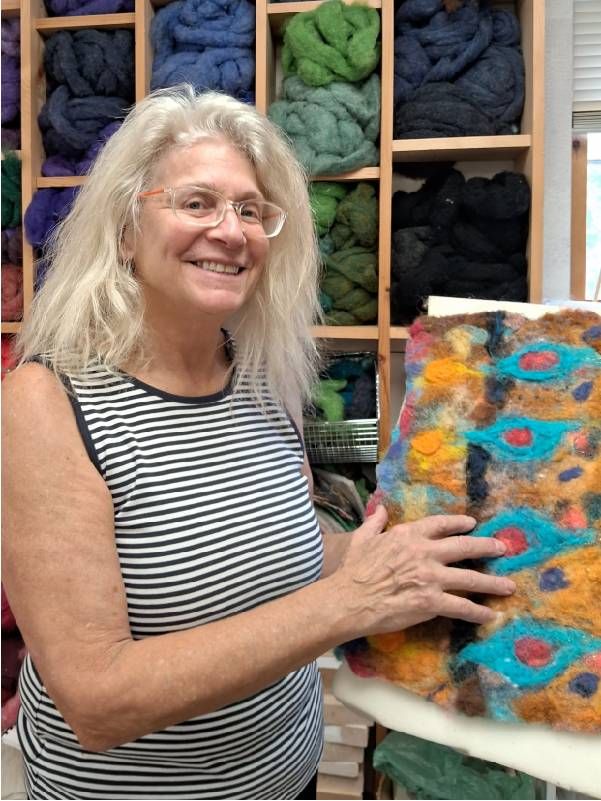 A woman holding up a piece of colorful fiber art. Next Avenue, Maine, Artists