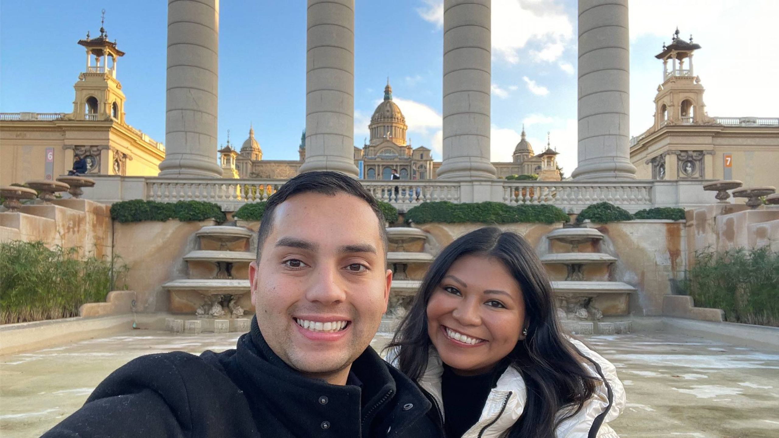 Two people smiling in front of ornate buildings. Next Avenue