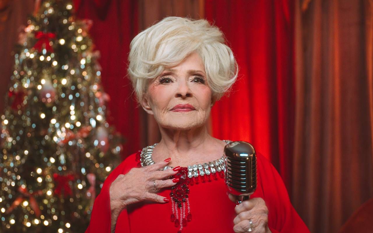 Brenda Lee wearing a red dress and holding a microphone in front of a Christmas tree. Next Avenue