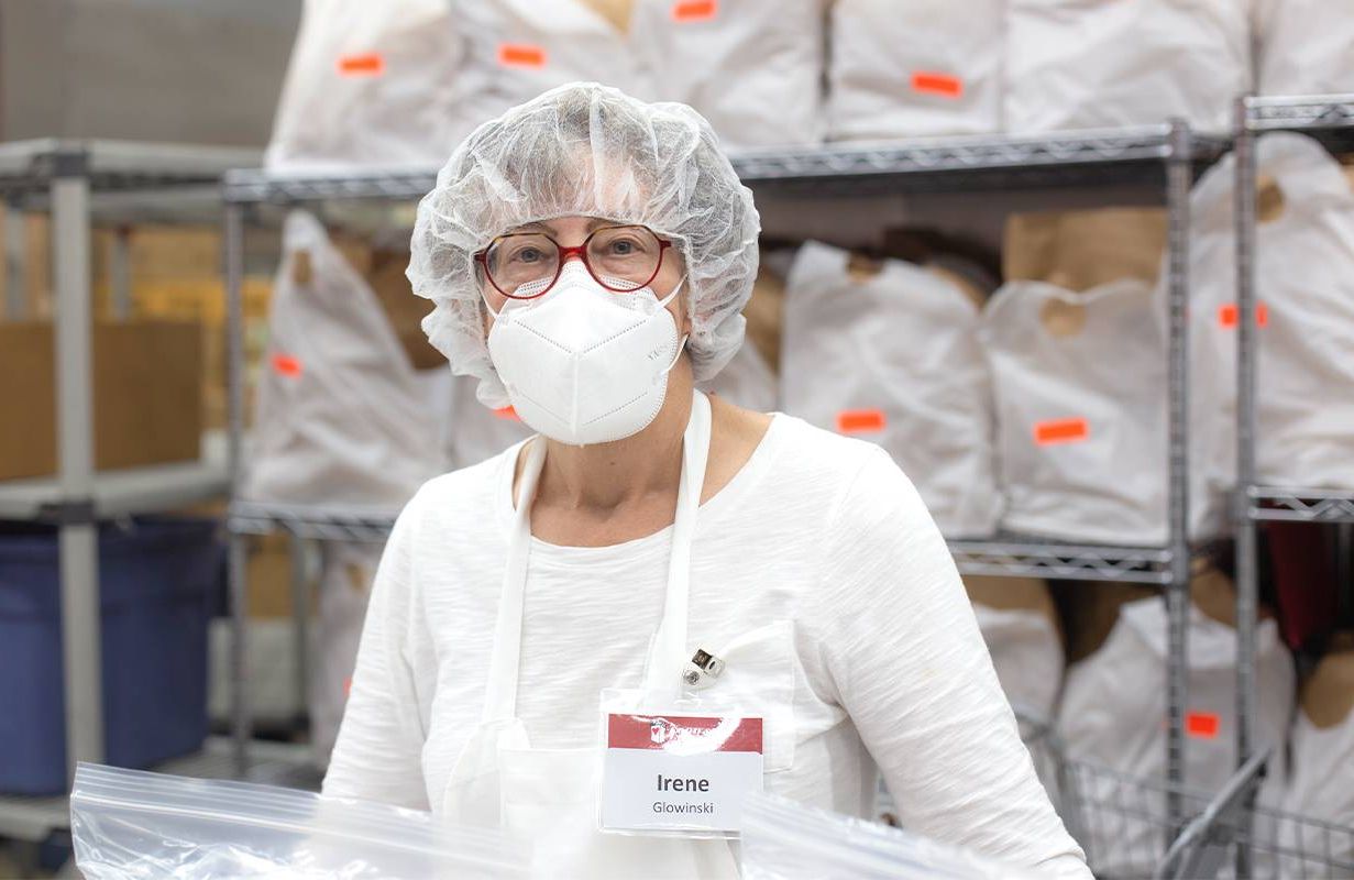 A woman wearing a face mask and hairnet working in a kitchen. Next Avenue