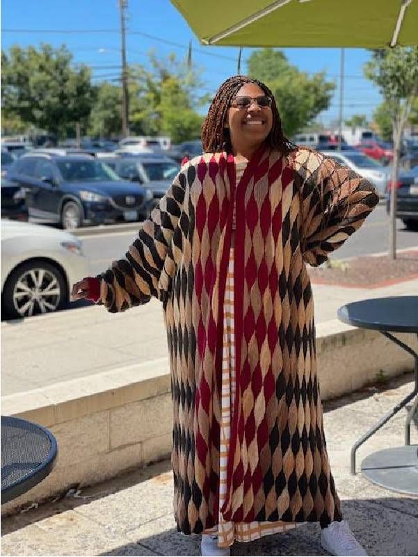 A person smiling and wearing a floor length, handmade, jacket. Next Avenue, quilting, The Loose Ends Project