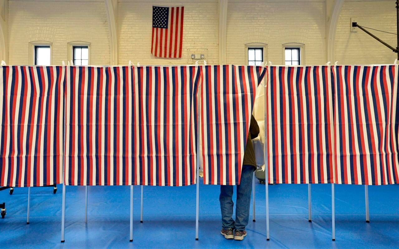 A person standing inside a covered voting booth in a community center. New Hampshire, primary, Next Avenue