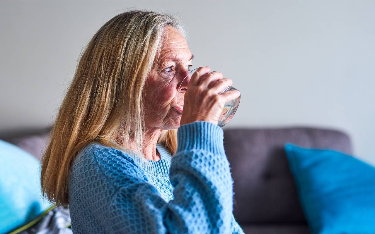 A middle aged woman drinking a glass of water. Next Avenue