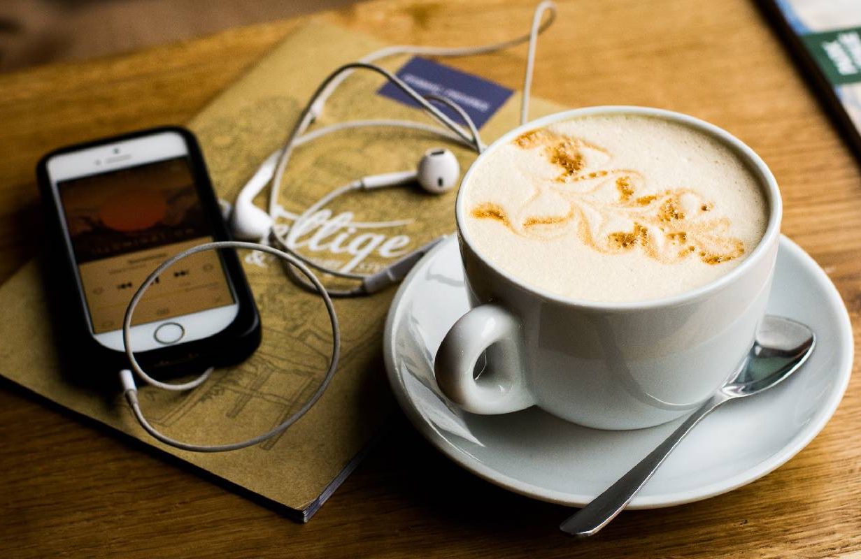 A mug of coffee next to a cellphone playing a podcast. Next Avenue