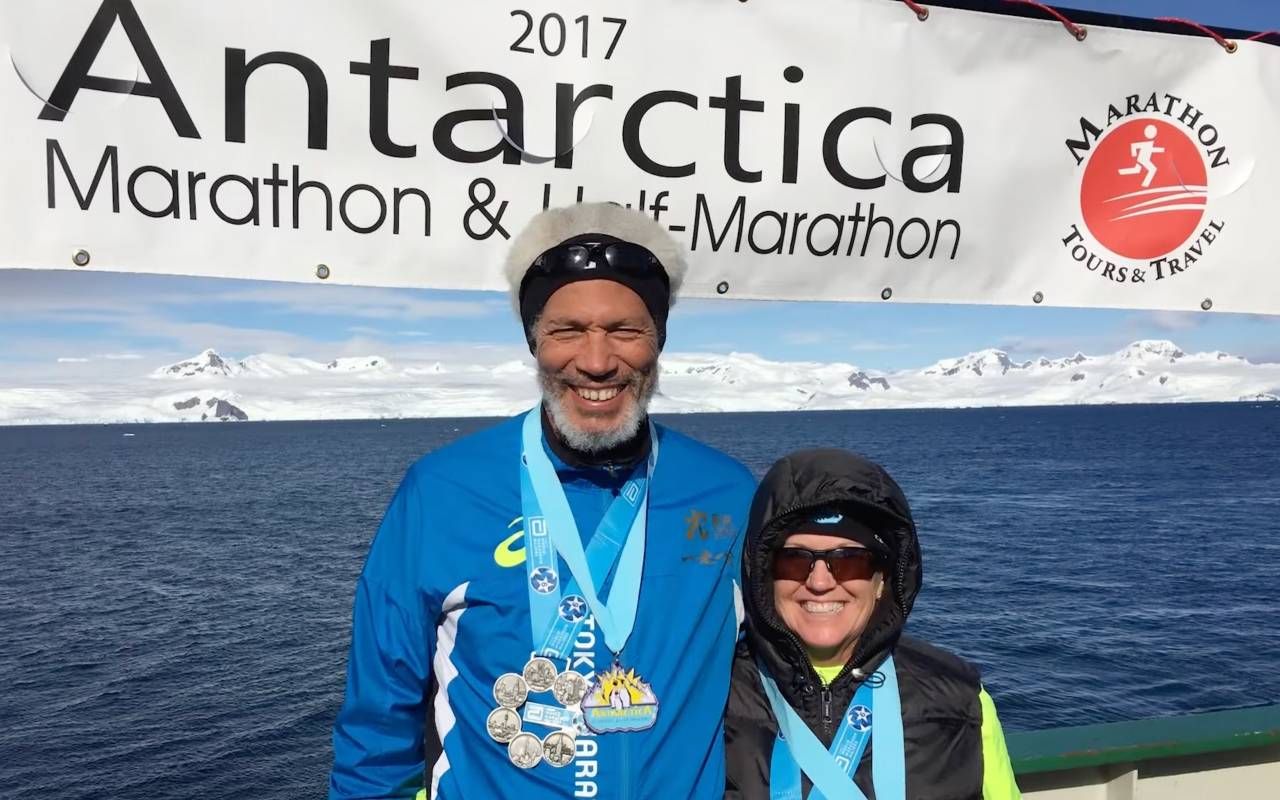 A couple smiling in front of a glacier after running a marathon in Antarctica. Next Avenue, running with cat