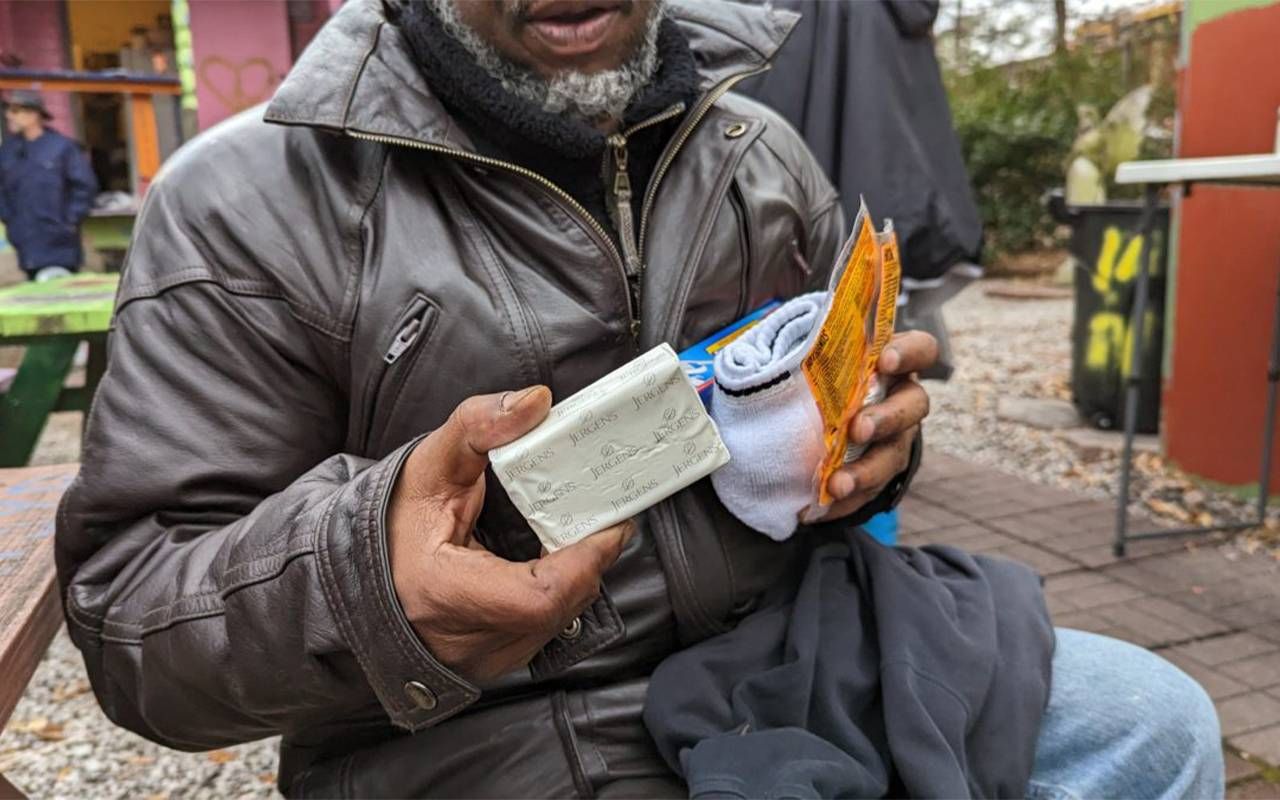 A man holding up various hygiene essentials like soap and clean socks. Next Avenue, homelessness, homeless older adults