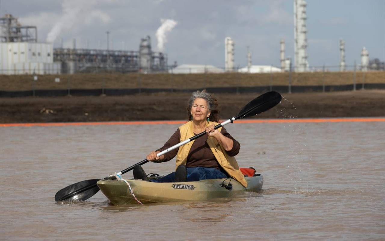 A woman kayaking with a power plant behind her. Next Avenue