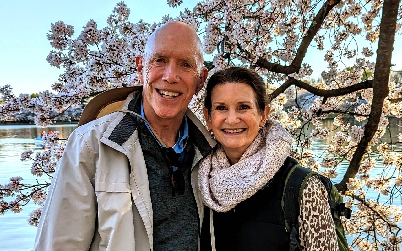 A couple smiling in front of a cherry blossom tree. Next Avenue