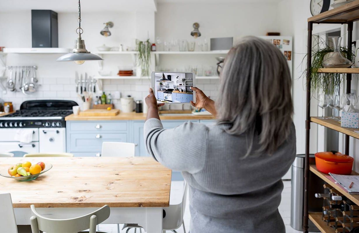 A woman taking photos of her kitchen preparing to sell her house. Next Avenue, capital gains tax