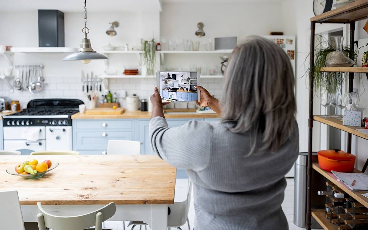 A woman taking photos of her kitchen preparing to sell her house. Next Avenue, capital gains tax