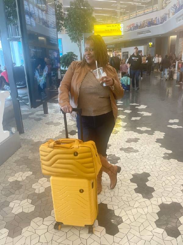 A woman standing in an airport with two yellow suitcases. Next Avenue