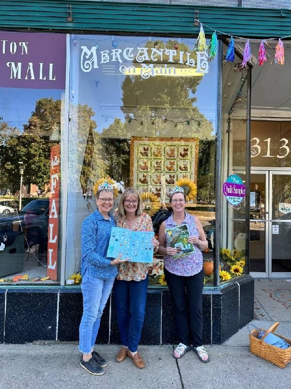 Three people smiling outside of a quilt store. Next Avenue, quilting