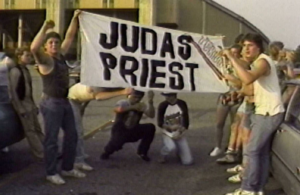 A vintage image of young people holding up a "Judas Priest" poster. Next Avenue, Heavy Metal Parking Lot