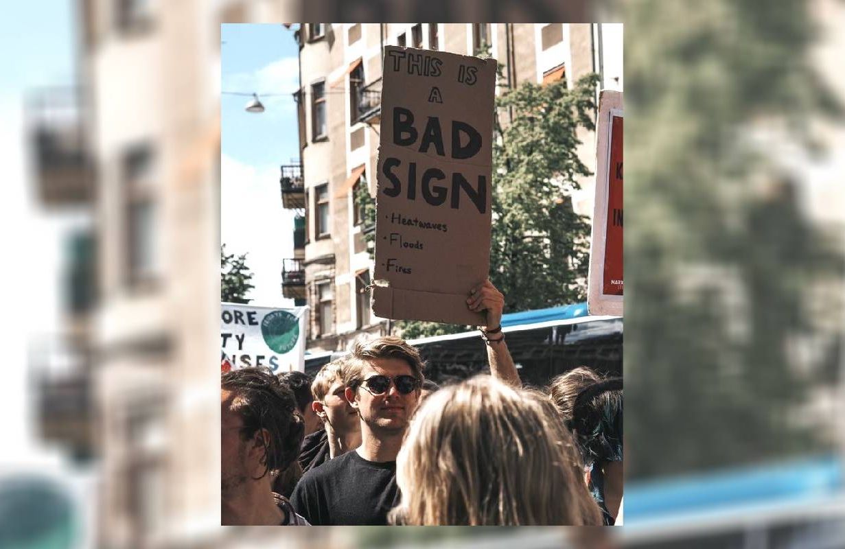 A young man holding up a climate activism related sign at a protest. Next Avenue, startups