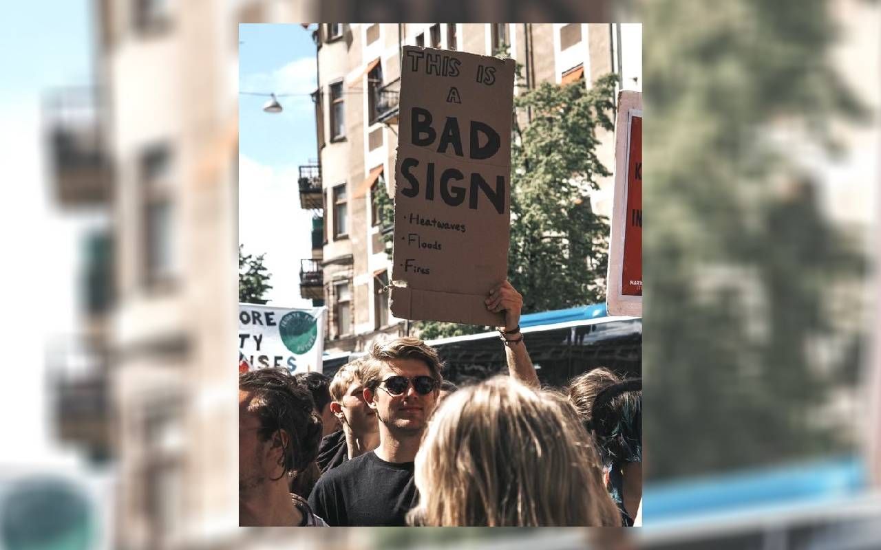 A young man holding up a climate activism related sign at a protest. Next Avenue, startups