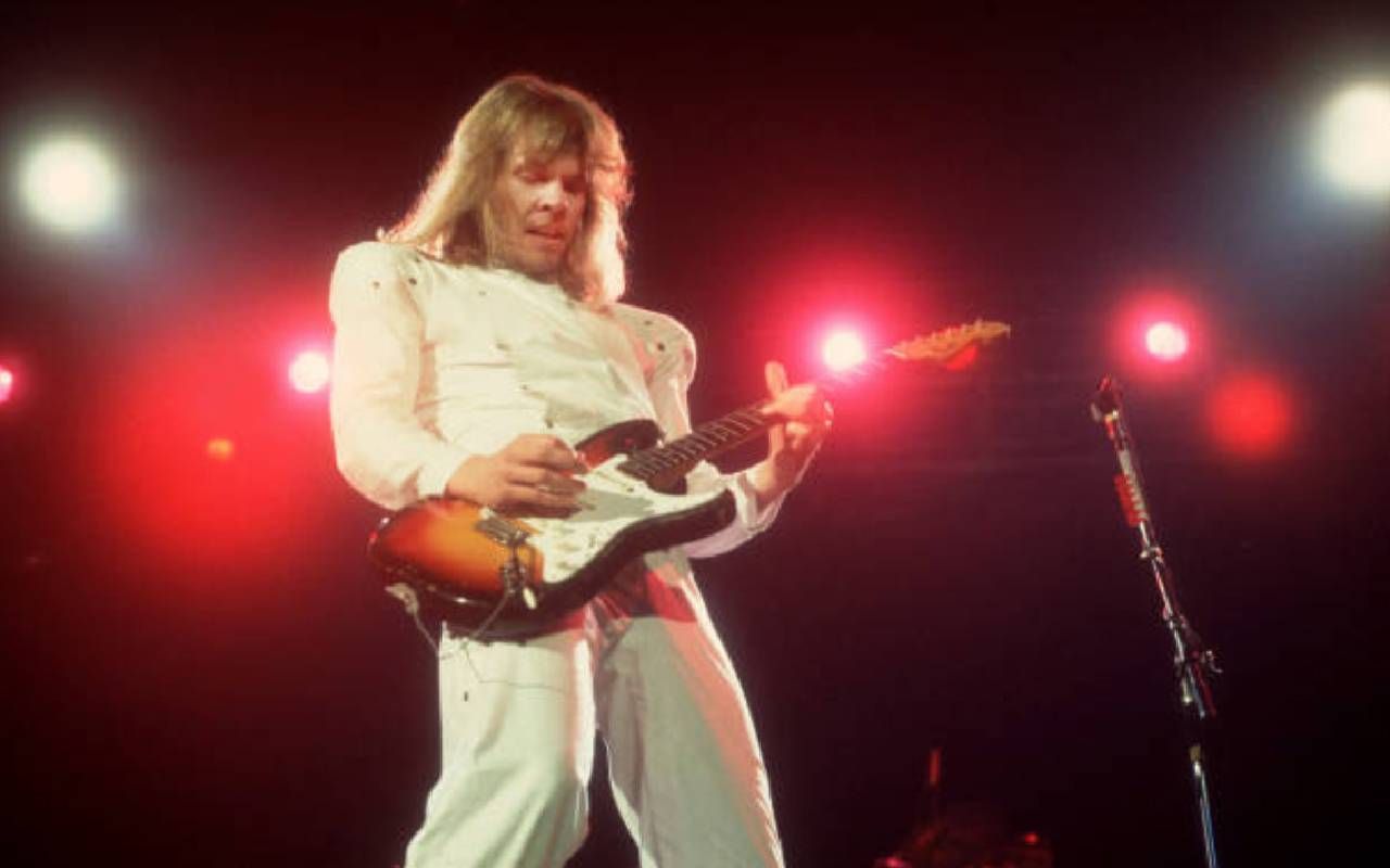 James Young wearing a white suit playing guitar on stage with Styx. Next Avenue