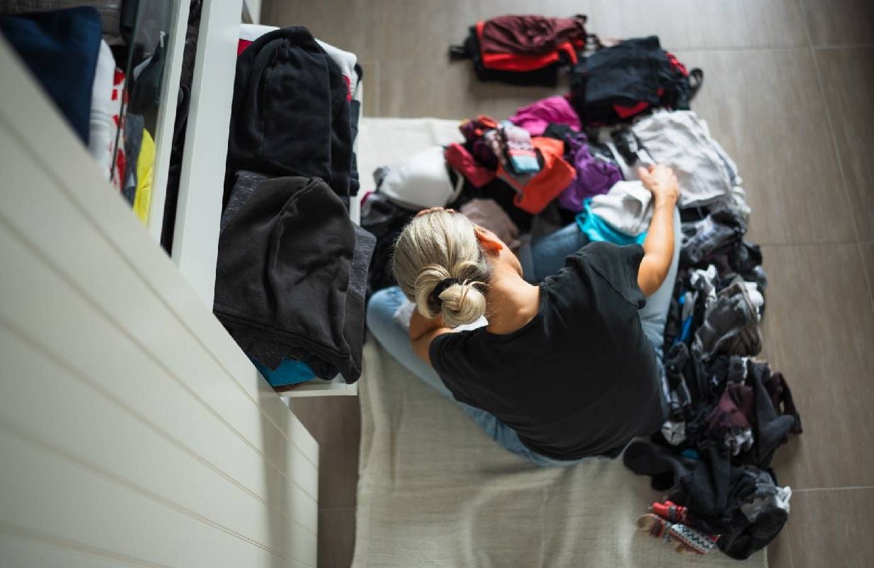 A woman looking frustrated with a pile of clothing after doing Swedish death cleaning. Next Avenue, life lift