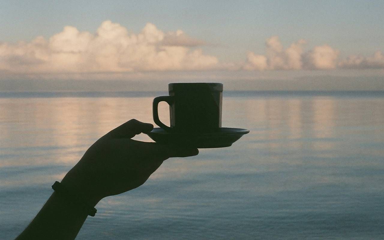 A person holding a cup of coffee with the ocean in the background. Next Avenue, caffeine, pros and cons