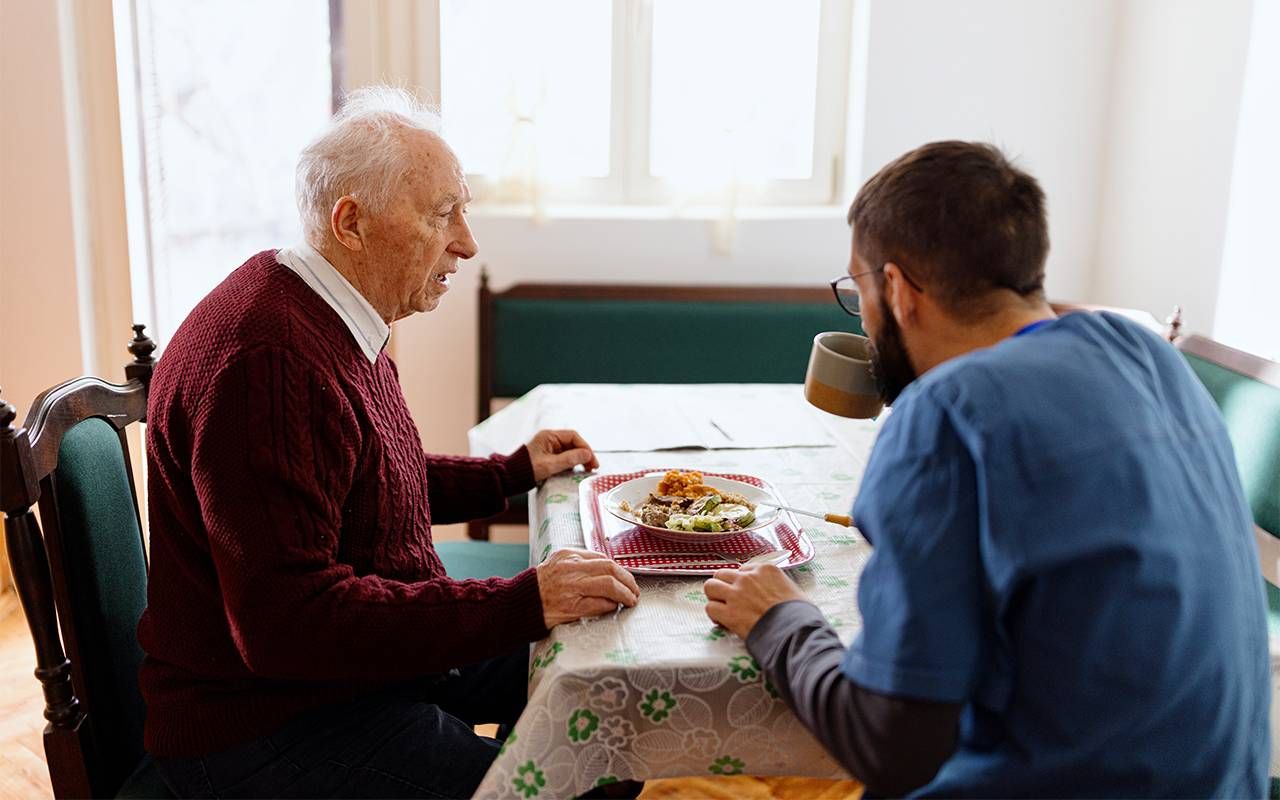 A caregiver with an older man sitting at the table. Next Avenue, hiring home care worker, caregiving