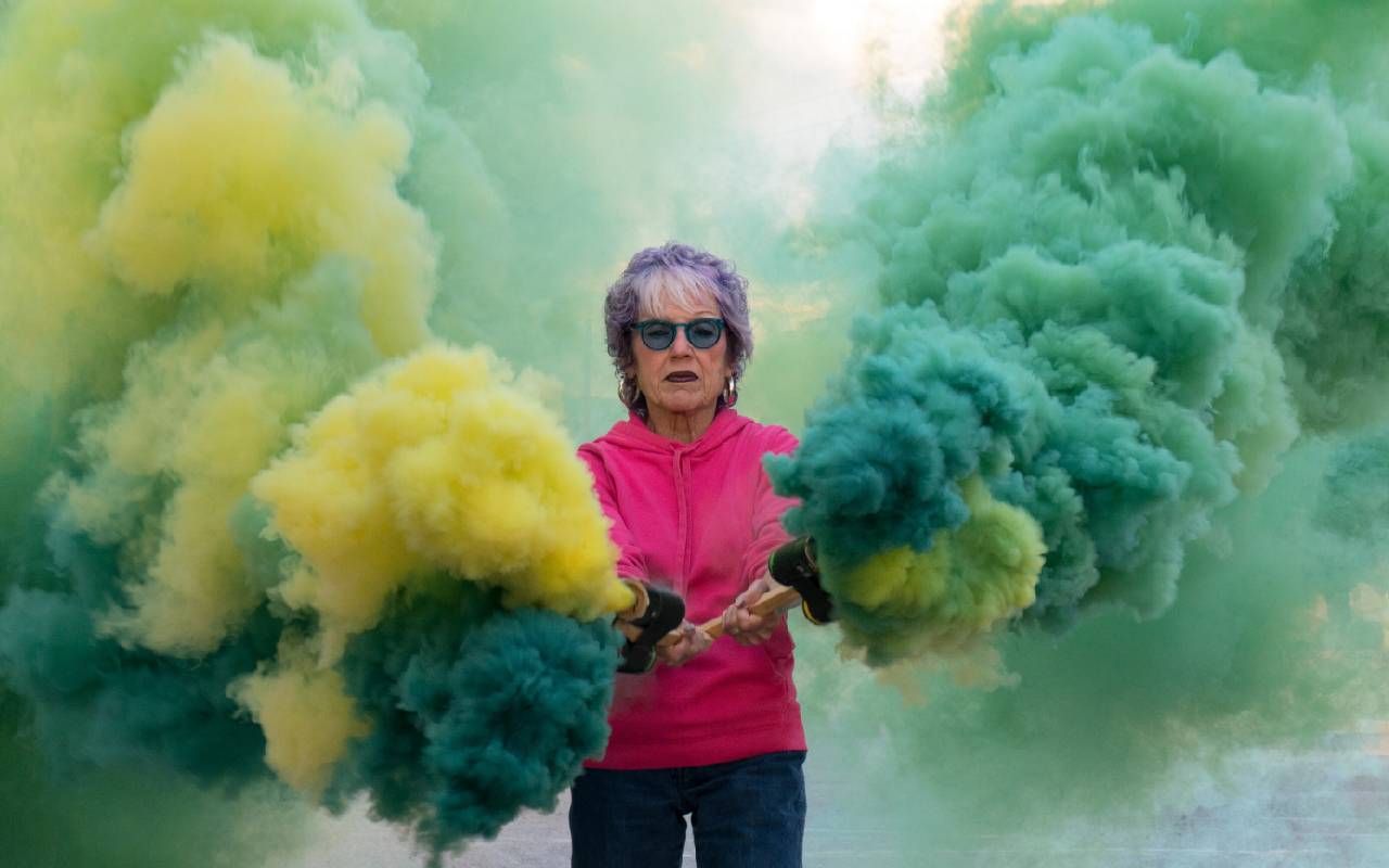 Artist Judy Chicago surrounded by colorful smoke. Next Avenue