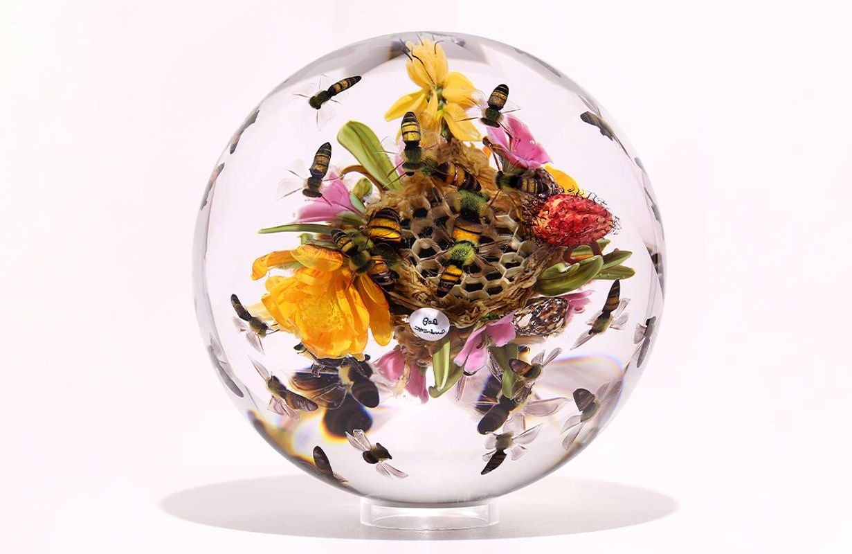 A glass ball with honeycomb, bees and flowers inside. Next Avenue, glass art, Paul Stankard