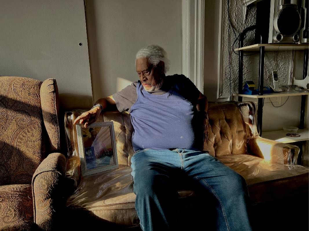 An older man sitting on a couch with a plastic slipcover. Next Avenue