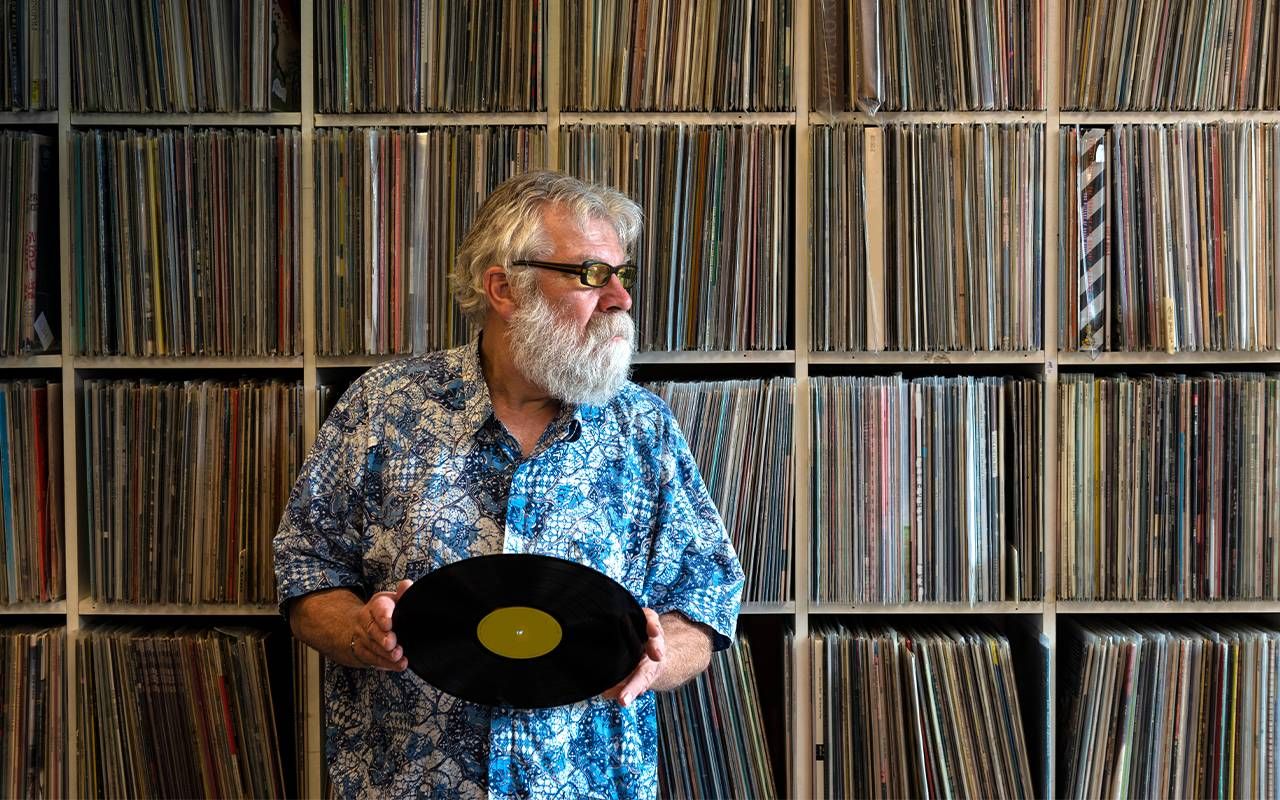 A man standing in front of a collection of vinyl records. Next Avenue