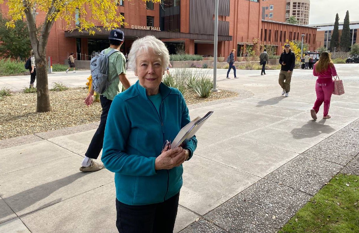 An older adult holding books while walking to class on a college campus. Next Avenue