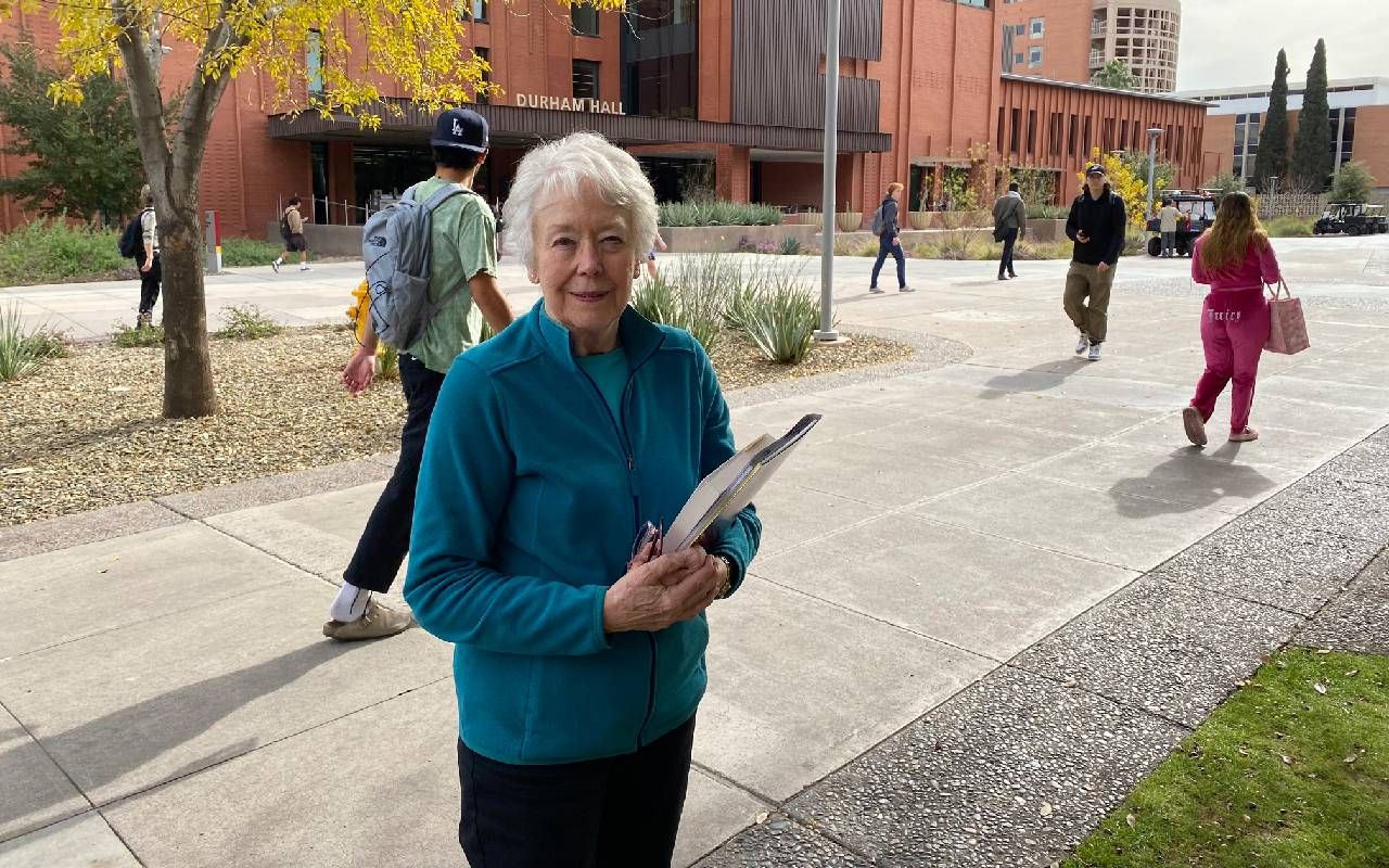 An older adult holding books while walking to class on a college campus. Next Avenue