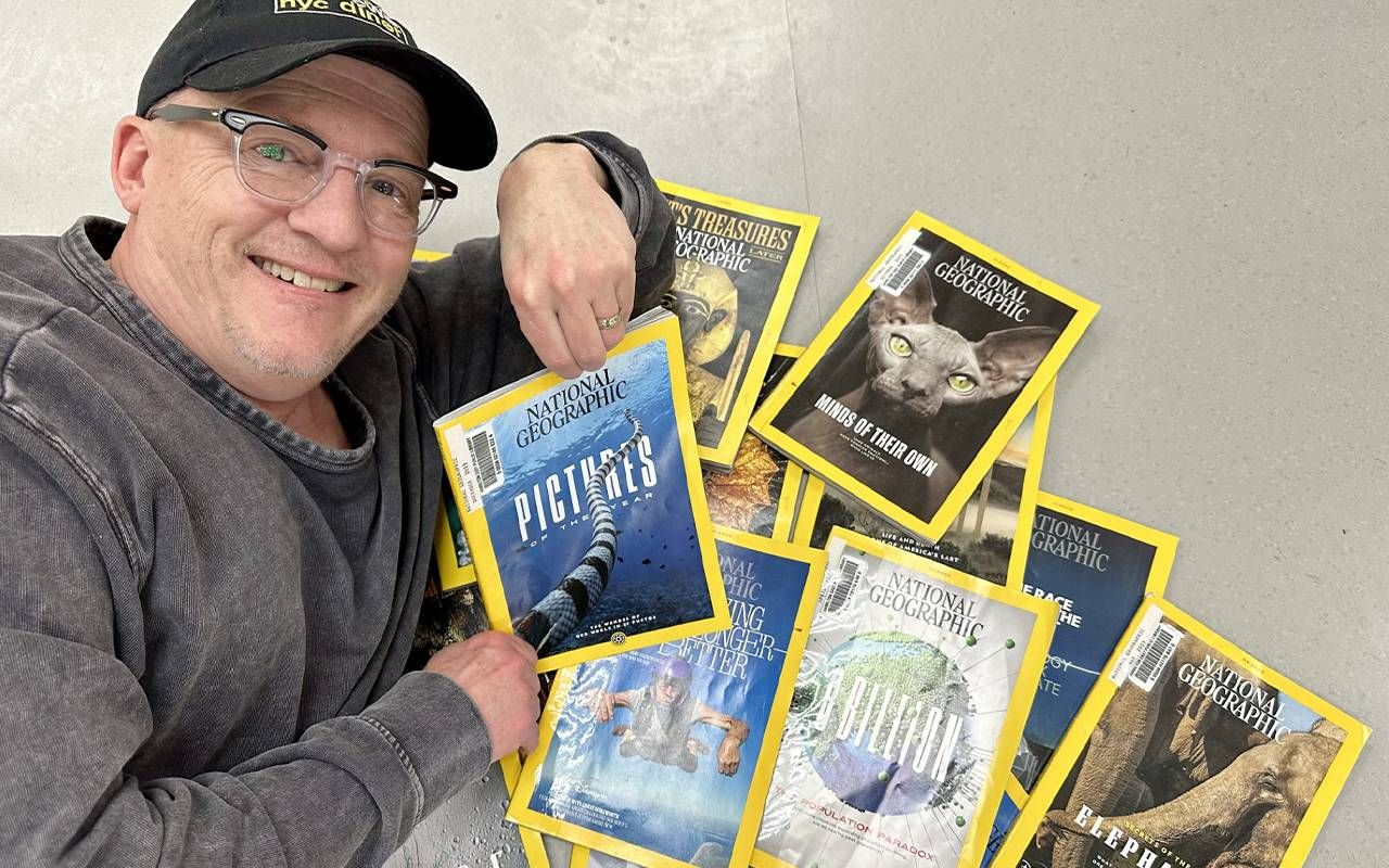 A man posing with national geographic magazines. Next Avenue