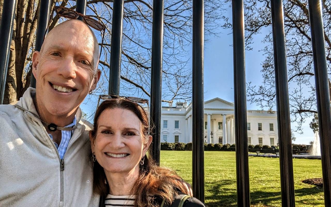 A couple smiling in front of the white house. Next Avenue, social security benefits 62