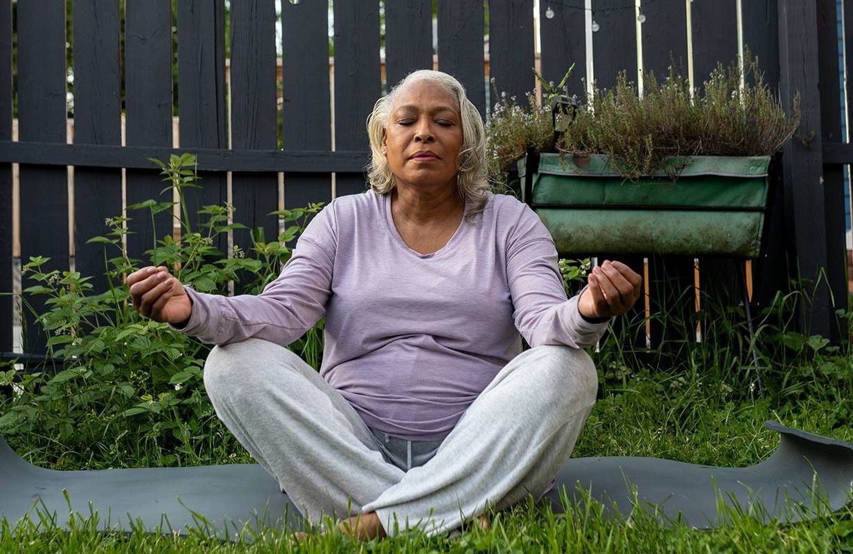 A woman meditating in her backyard. Next Avenue