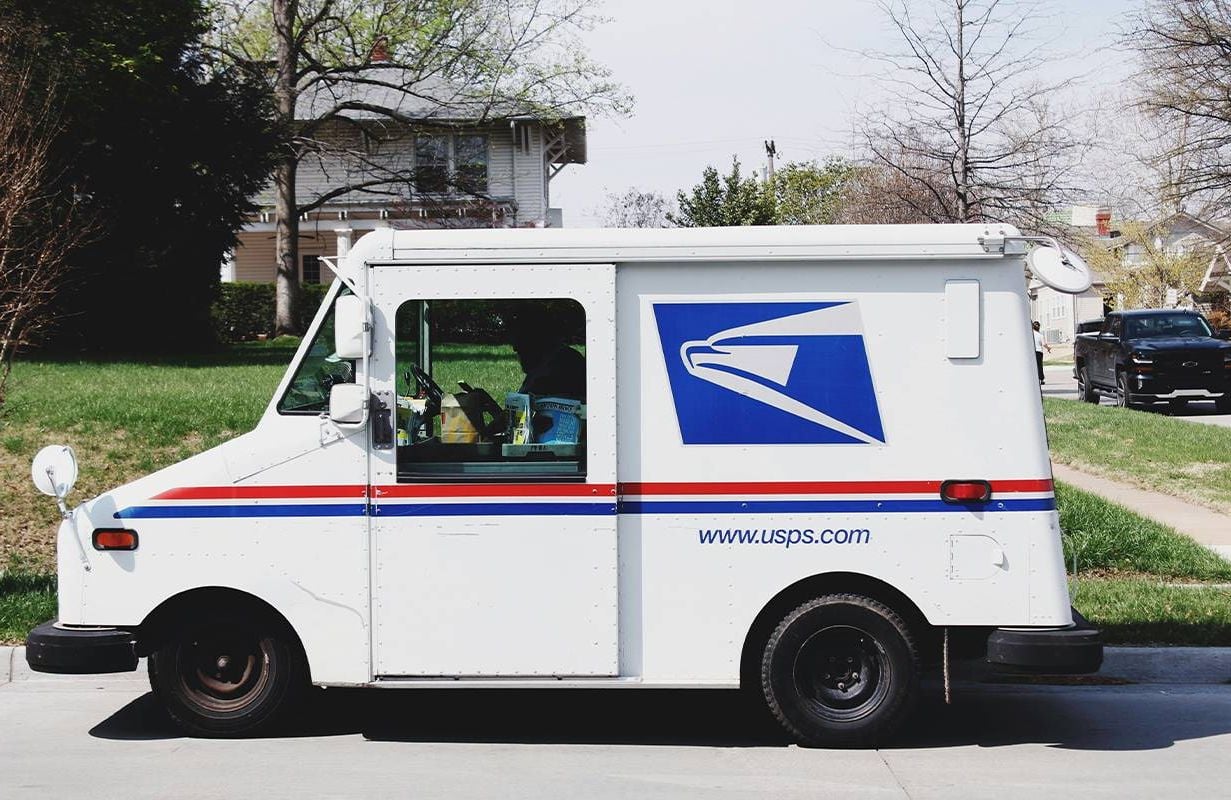 A USPS truck putting mail in a mailbox. Next Avenue, college admissions junk mail