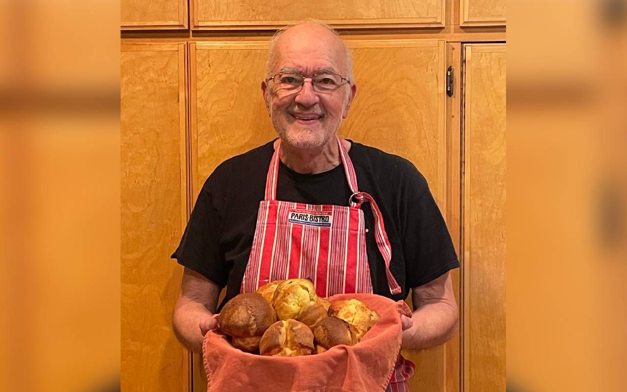 A man wearing an apron and holding a basket full of popovers