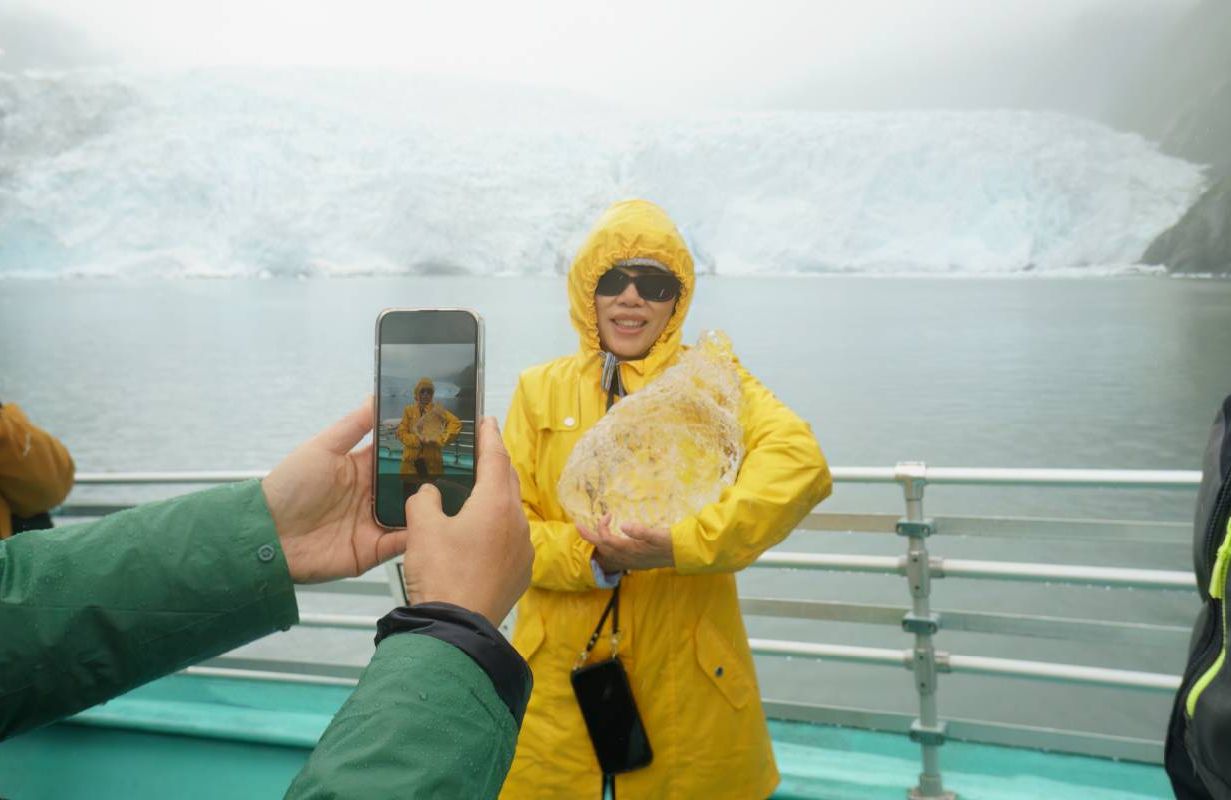 A person posing with a chunk of glacier ice. Next Avenue, reverse snowbird