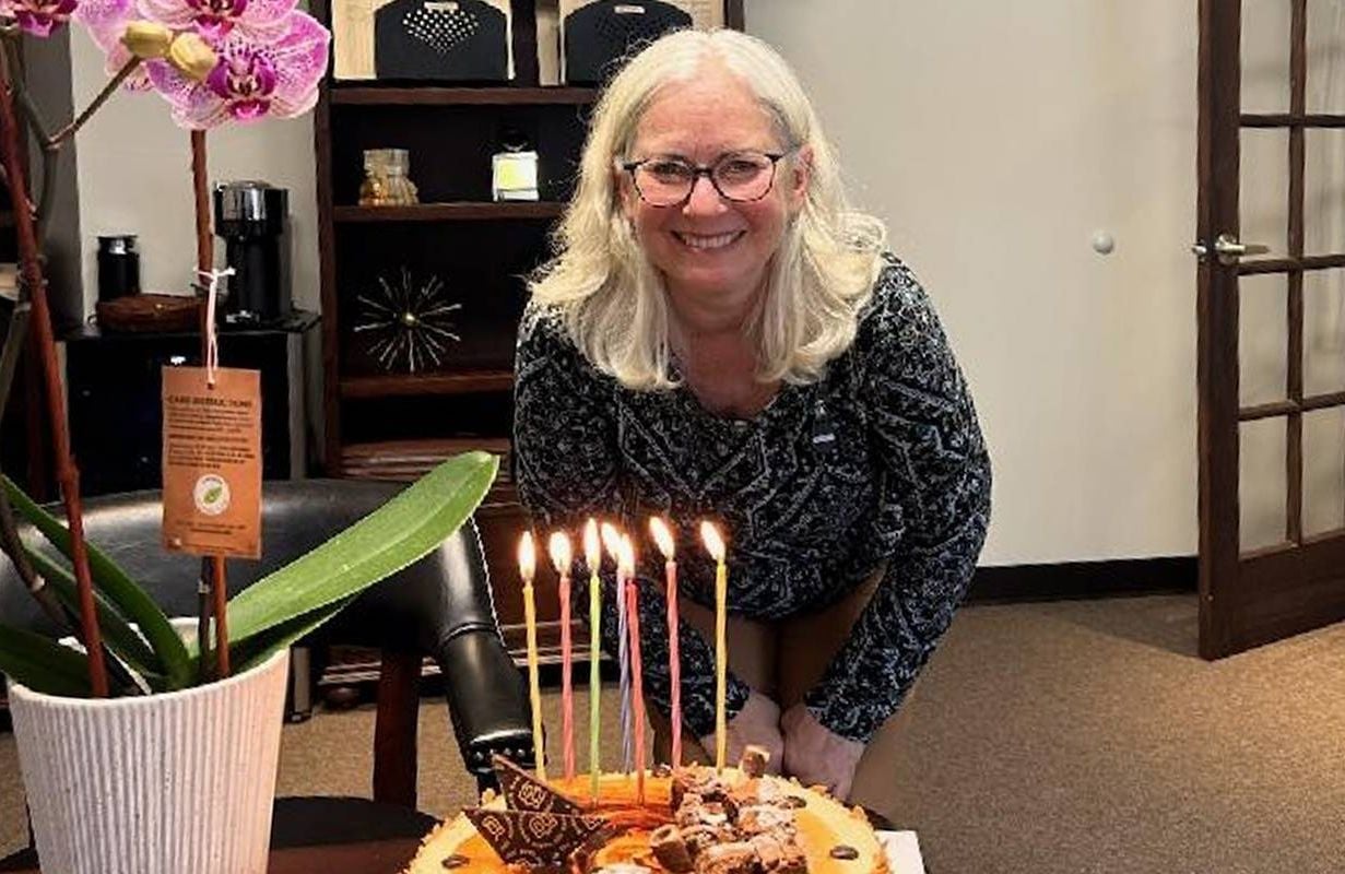 A person smiling in front of a birthday cake. Next Avenue, turning 70