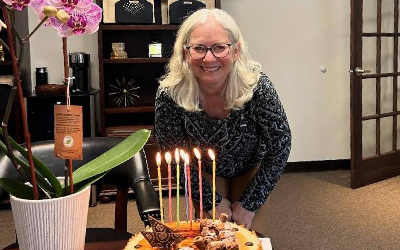 A person smiling in front of a birthday cake. Next Avenue, turning 70