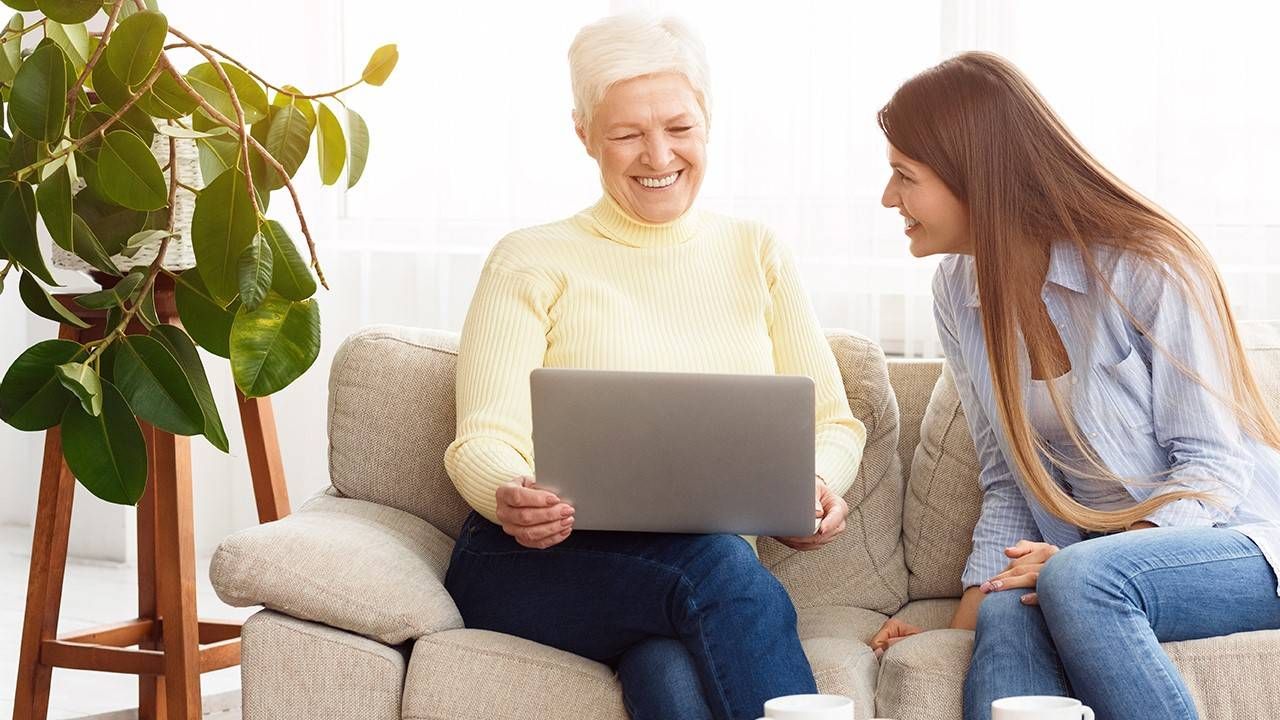 An older parent using a laptop and talking to her adult child.