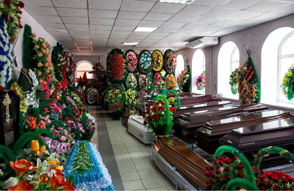 The interior of a funeral accessories store that is selling coffins and various flower arrangements. Next Avenue