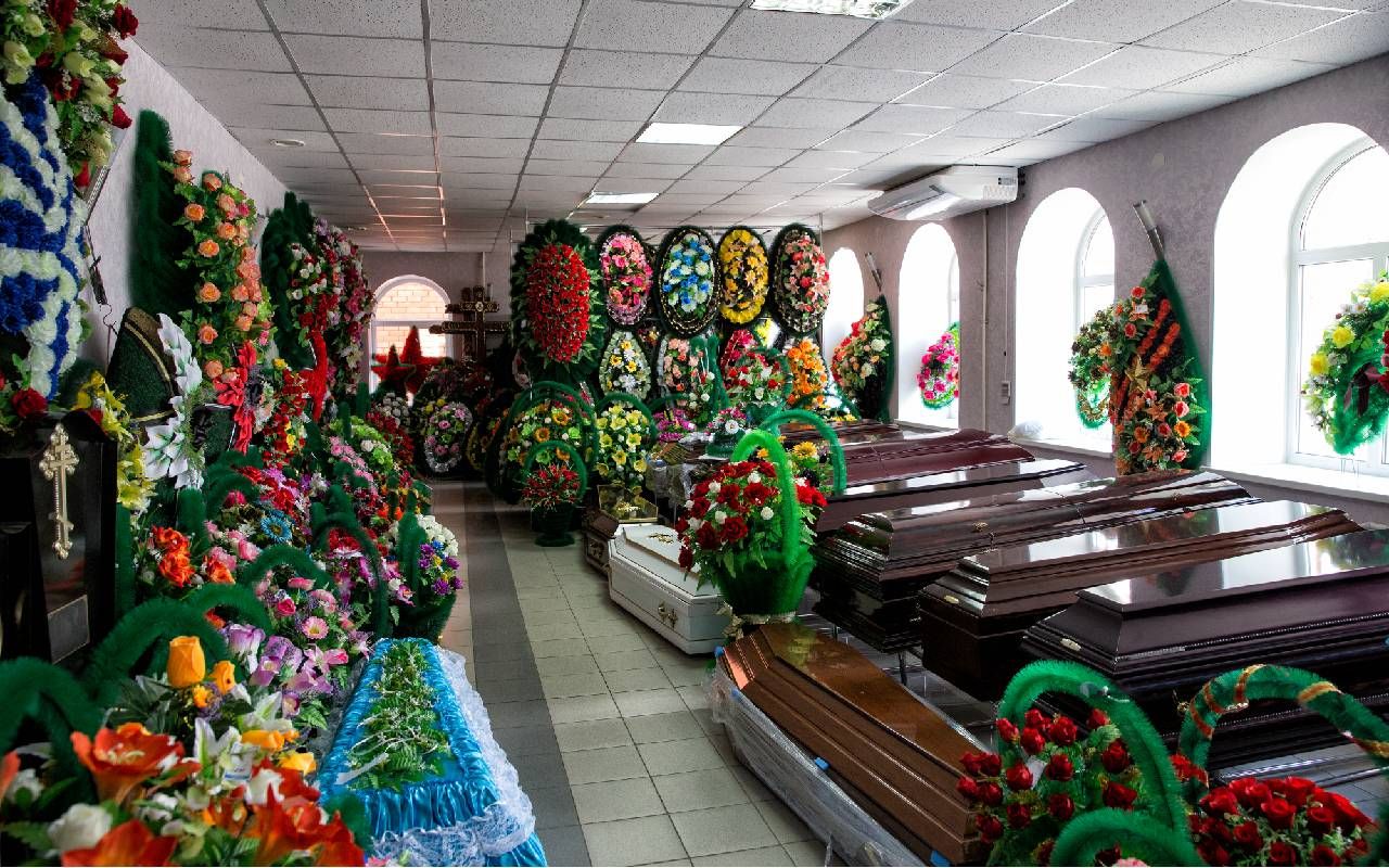 The interior of a funeral accessories store that is selling coffins and various flower arrangements. Next Avenue