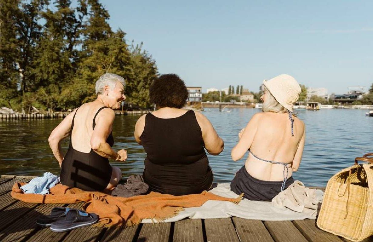 Three friends who are aging gracefully laughing together on a dock. Next Avenue